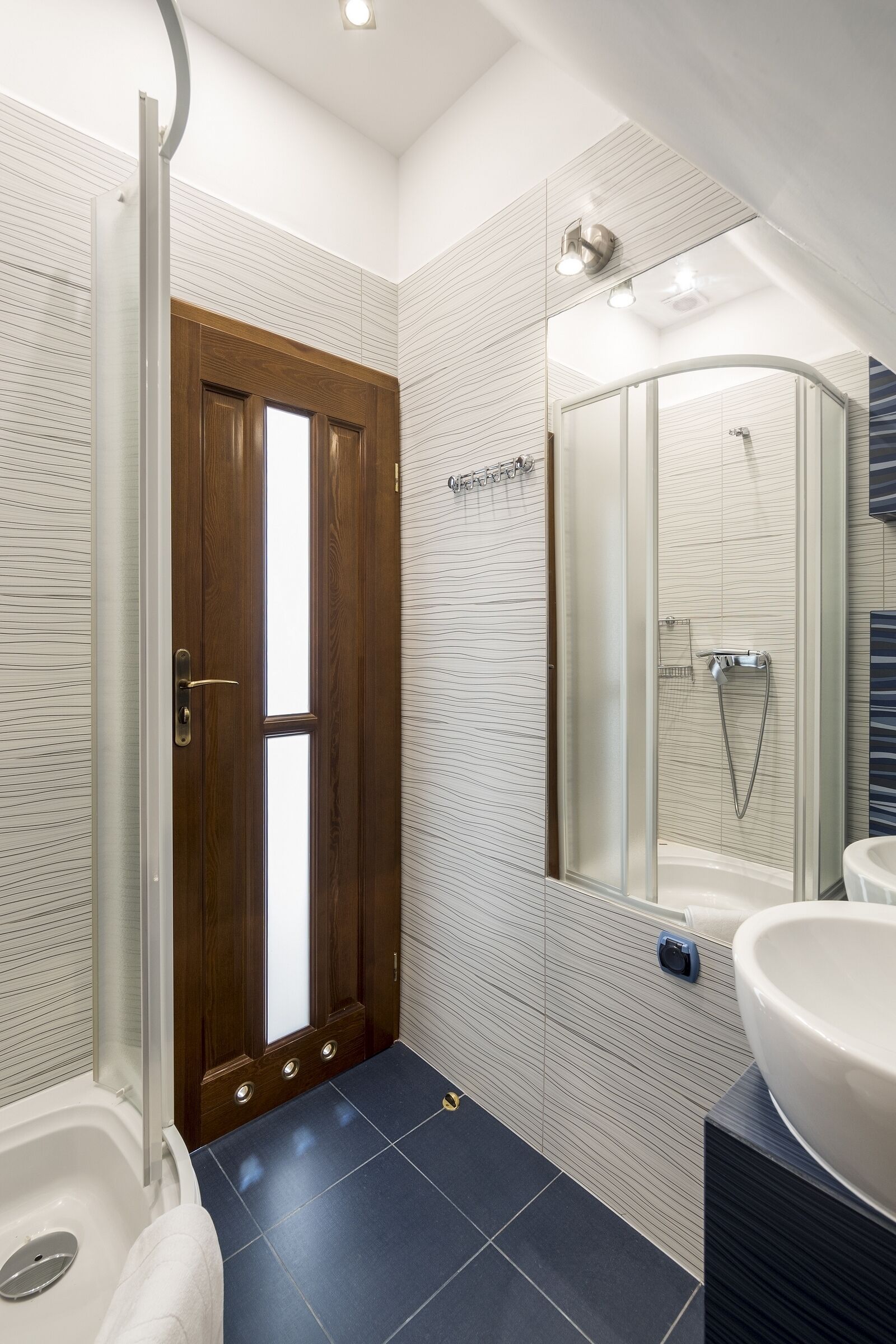 A modern bathroom with a glass shower enclosure, a white bathtub, and a large mirror above the sink.