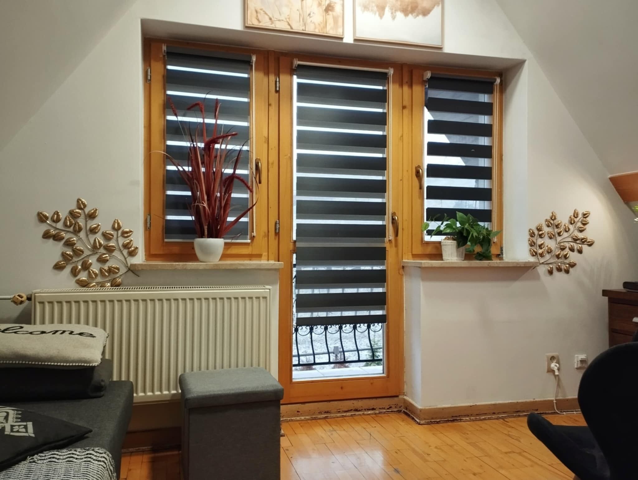 Una habitación con techo inclinado, un radiador, un sofá, una mesita y una ventana con persianas.