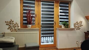Una habitación con techo inclinado, un radiador, un sofá, una mesita y una ventana con persianas.