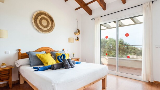 Een slaapkamer met een houten bed, een nachtkastje, een wandlamp en een grote glazen schuindeur die leidt naar een balkon.