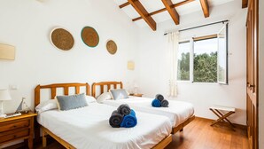 Een kamer met twee bedden, houten hoofdborden, wit beddengoed en een raam met gordijnen.