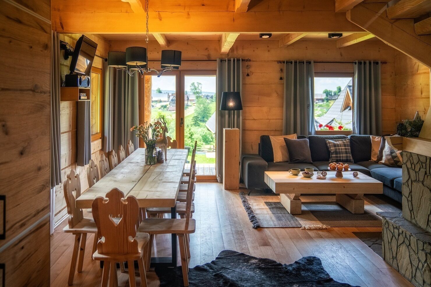 A cozy wooden cabin interior with a dining area, sofa, and a view of the outdoors.