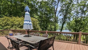 Una terraza de madera con una mesa, sillas y una sombrilla, con vistas a un lago.