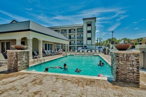 A pool area with a clear blue sky, a building with multiple balconies, and a brick poolside.