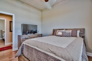 A bedroom with a large bed, a TV on a wooden dresser, and a red rug on the floor.
