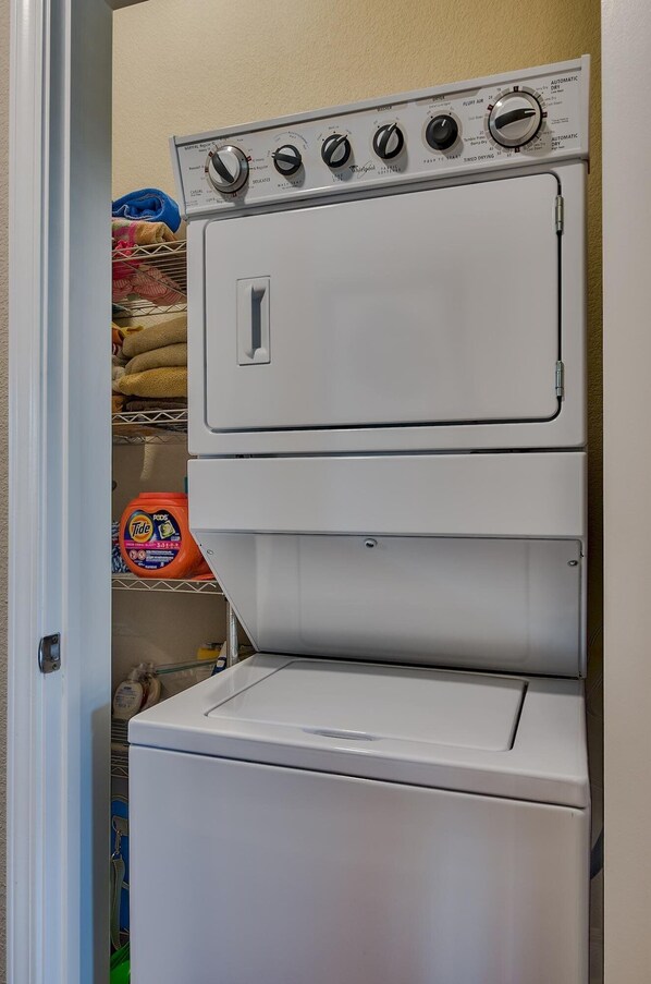 A stacked washer and dryer unit with control knobs and a detergent bottle visible in the background. - ALERIO UNIT B301 for 8 Guests with Pool & Jacuzzi (Miramar Beach)