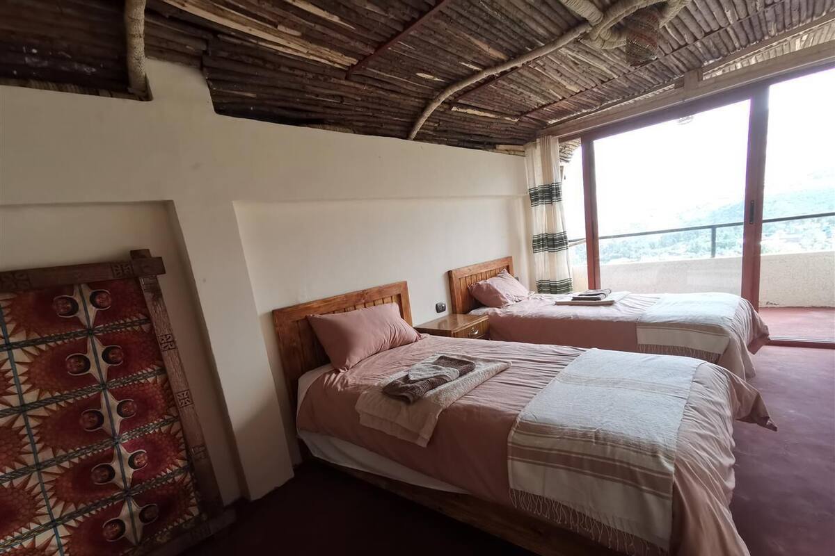 Une chambre avec deux lits, un plafond en bois et une grande fenêtre.