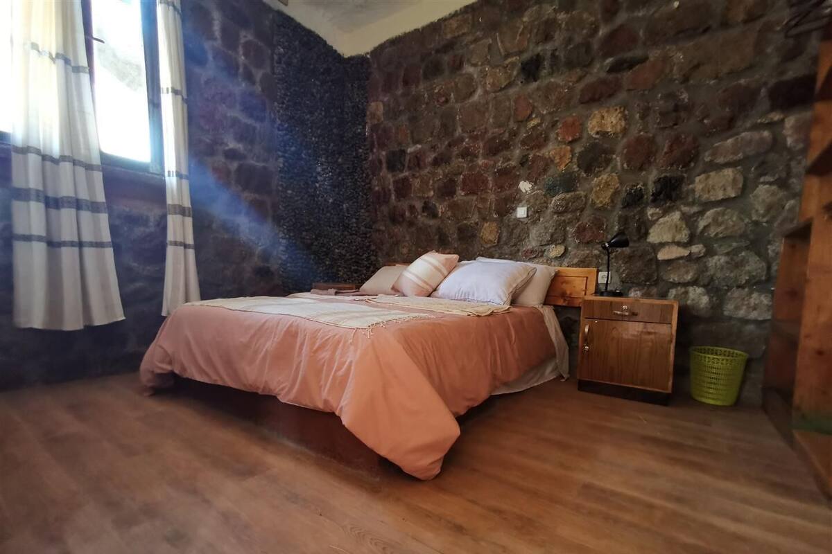 Une chambre avec un mur en pierre, un plancher en bois et un lit recouvert d’une couverture rose.