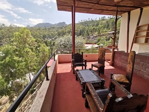 A balcony with a red floor, wooden furniture, and a view of a green landscape with trees and hills. - Lalibela Apartments (Lalibela)