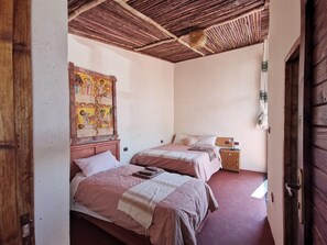 Ein Zimmer mit zwei Betten, einer Holzbalkendecke und einer Wand mit einem bunten Wandteppich.