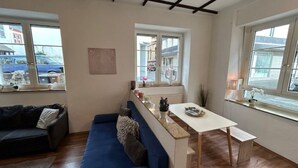 Een moderne woonkamer met een blauwe bank, een eettafel en een keuken met een raam.