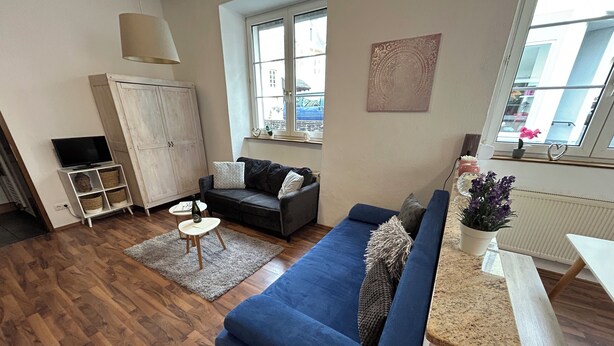 Een moderne woonkamer met een blauwe bank, een klein rond tafeltje, een kast en een raam met uitzicht.
