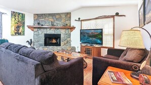 Een woonkamer met een stenen openhaard, een televisie, een bank, een salontafel en een lamp.