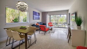 A modern living room with a dining area, large windows, and a balcony with plants. - The Elmar Boutique Hotel (Lauderdale-by-the-Sea)