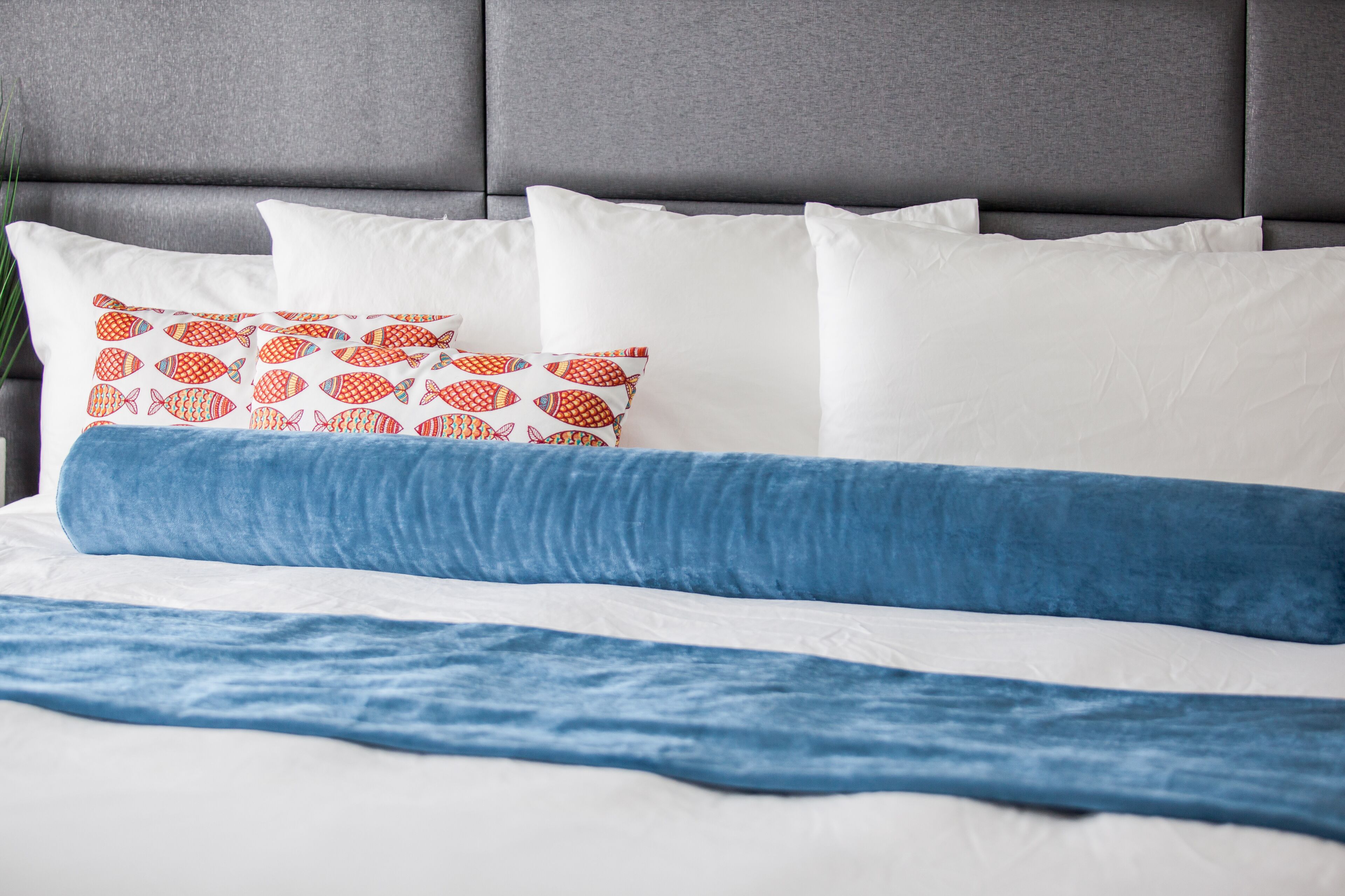 A bed with white and blue bedding, a grey upholstered headboard, and a patterned pillow.
