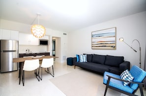 Ein modernes Wohnzimmer mit einer schwarzen Couch, einem blauen Sessel und einem Esstisch mit weißen Stühlen.