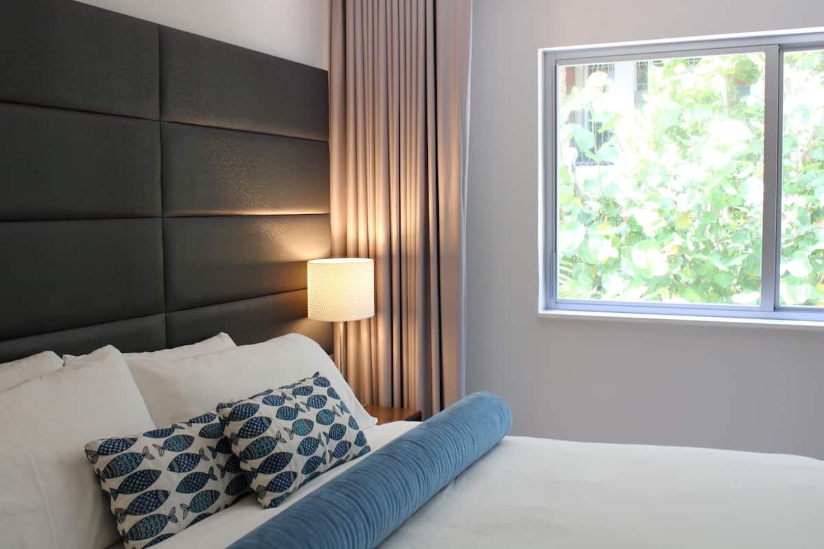Una habitación de hotel con cama, cabecero, ventana y cortinas.