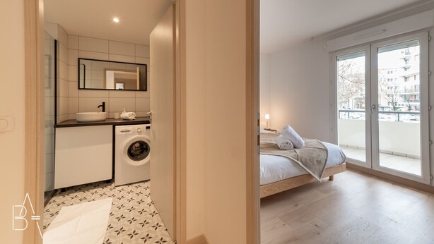 Un apartament modern amb bany, rentadora, llit i un balcó amb vistes a edificis.
