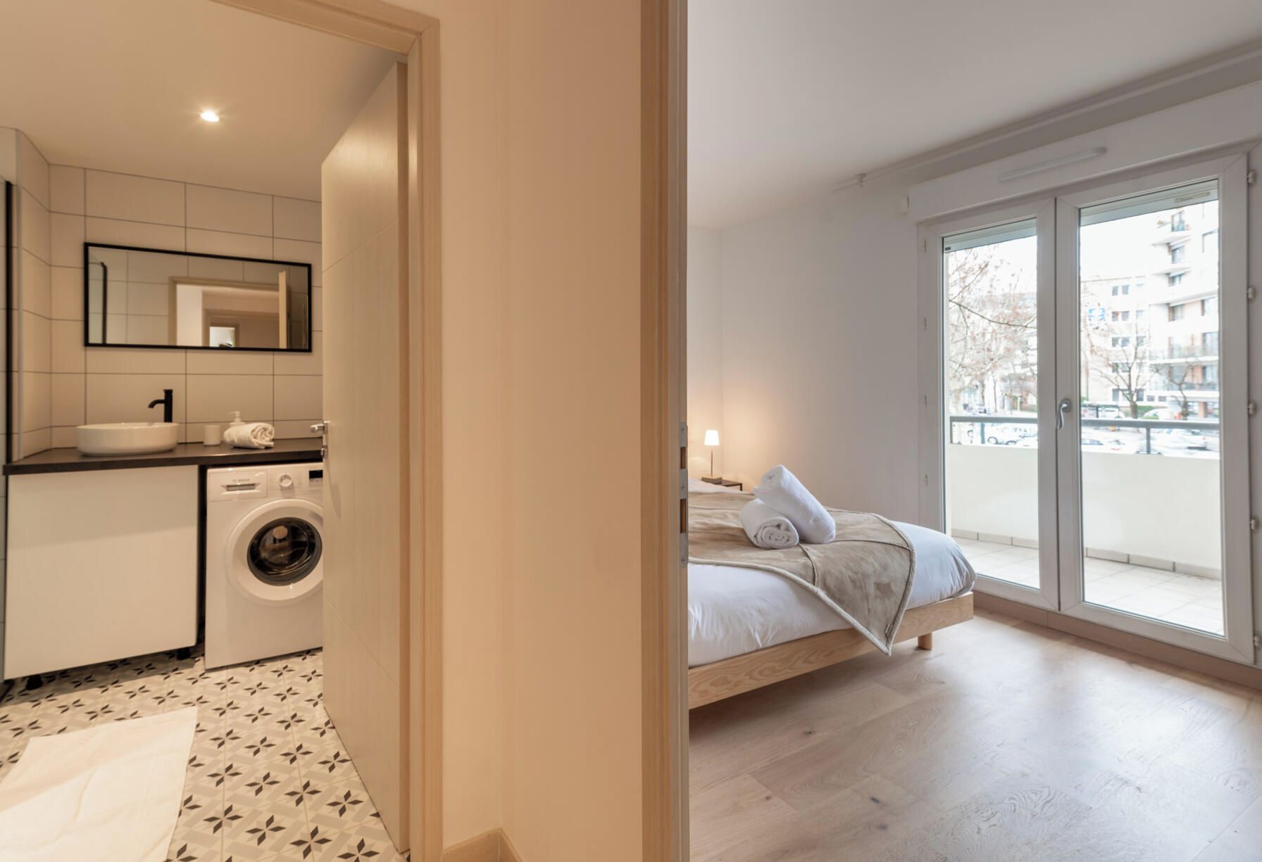 A modern apartment with a kitchen, a washing machine, a bed, and a balcony with a view.