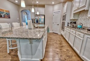 A kitchen with a granite countertop, white cabinets, and a dining area with chairs. - Coastal Club * 5 BR Luxury Beach House (Lewes)