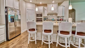 Una cocina con gabinetes blancos, electrodomésticos de acero inoxidable y taburetes de bar.