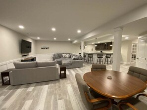 A modern living room with a sectional sofa, a dining table, and a kitchen area in the background.