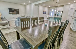 A dining area with a wooden table and chairs, a kitchen with white cabinets, and a TV mounted on the wall. - Coastal Club * 5 BR Luxury Beach House (Lewes)