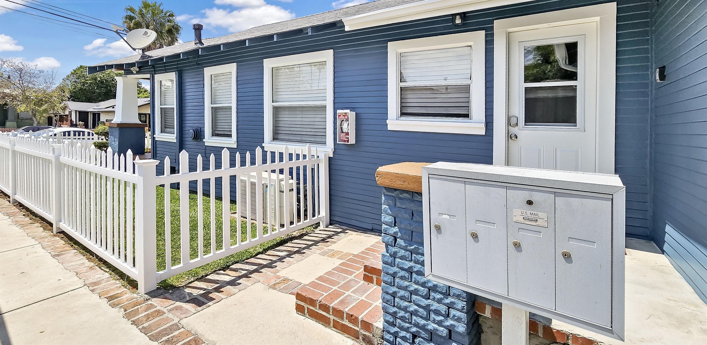 A residential building with a white picket fence, a mailbox, and a utility box.