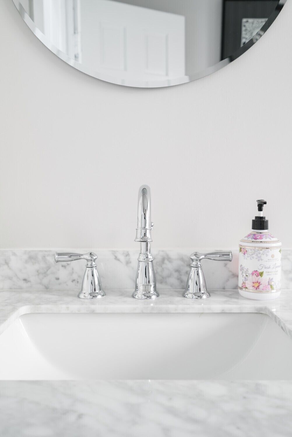 Une salle de bain avec un lavabo blanc, trois robinets chromés et un distributeur de savon à motifs floraux.