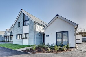 Un immeuble résidentiel moderne doté d’un toit en pente, d’un petit garage attenant et d’une pelouse bien entretenue.