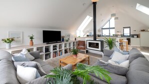 Ein großzügiges Wohnzimmer mit einem großen Fernseher, einem Kamin und einer Küche im Hintergrund.