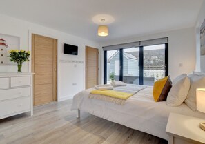 Relax in this serene bedroom with a large bed, a dresser, and a nightstand, offering a peaceful view from the large window.