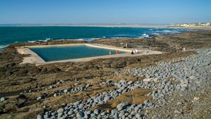 Ein felsiger Strand mit einem Schwimmbecken, umgeben von Kieselsteinen und freiem Blick auf den Ozean.