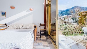 A bedroom with a bed, a small table, and a chair. There is a sliding glass door leading to a balcony with a view of the mountains. - Le Garibaldi - Studio cosy Sospel (Sospel)