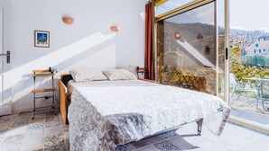 A bedroom with a large bed, a small table, and a view of a balcony with outdoor furniture. - Le Garibaldi - Studio cosy Sospel (Sospel)