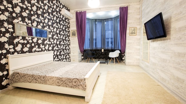 Un dormitorio con cama, televisor, ventana con cortinas y espejo en la pared.