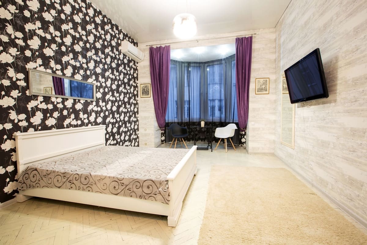 Quarto com cama, televisão, janela com cortinas e espelho na parede.