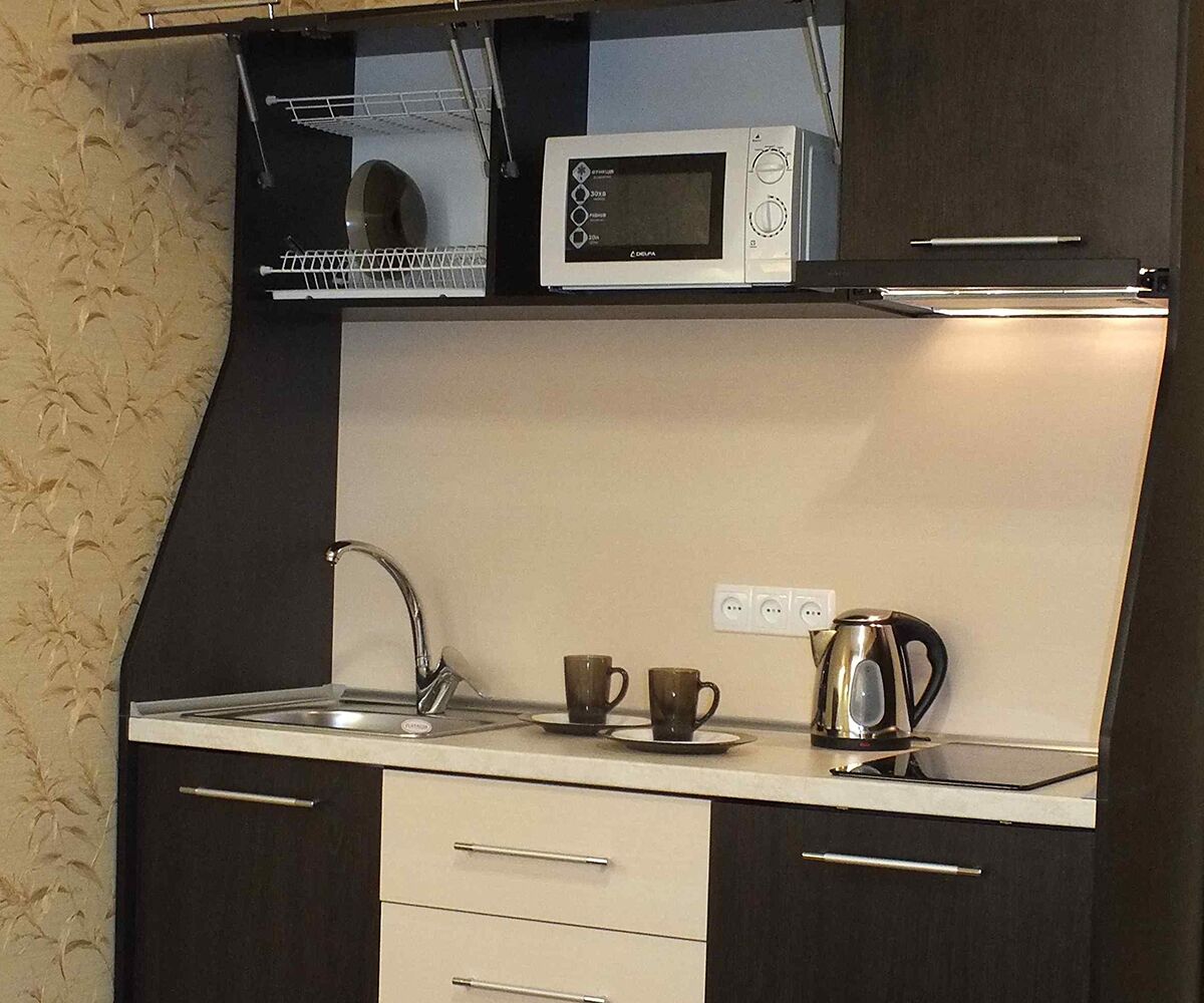 A compact kitchen with a microwave, kettle, and two cups on the counter.