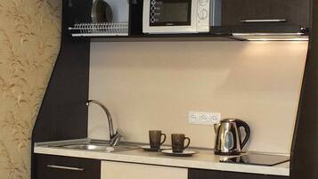 A compact kitchen with a microwave, kettle, and two cups on the counter.