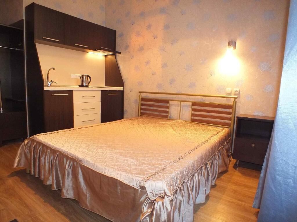 A bedroom with a bed, a nightstand, a dresser, and a small kitchenette area.