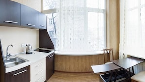 Una cocina compacta con un lavamanos, estufa y ventana con cortinas.