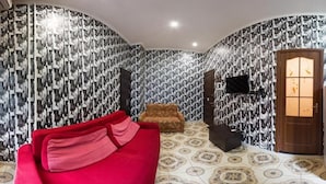 Una habitación con papel tapiz estampado, un sofá rojo, un sillón marrón y una puerta de madera con paneles de vidrio.