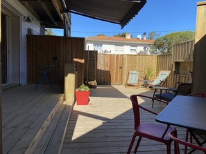 Ett trädäck med ett bord och stolar, en röd blomkruka med växter och en randig strandstol.