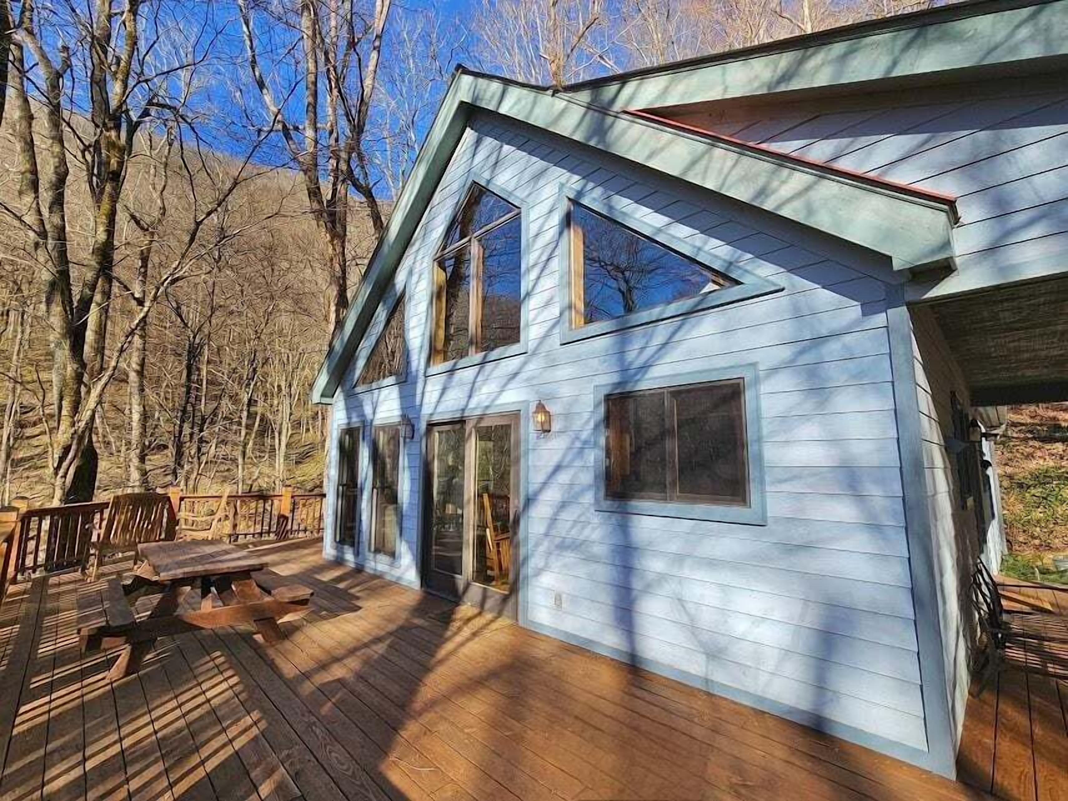 Una casa de dos pisos con un balcón, ventanas amplias y un paisaje de montañas al fondo.