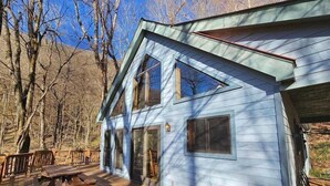 A two-story house with a deck, large windows, and a mountain backdrop.