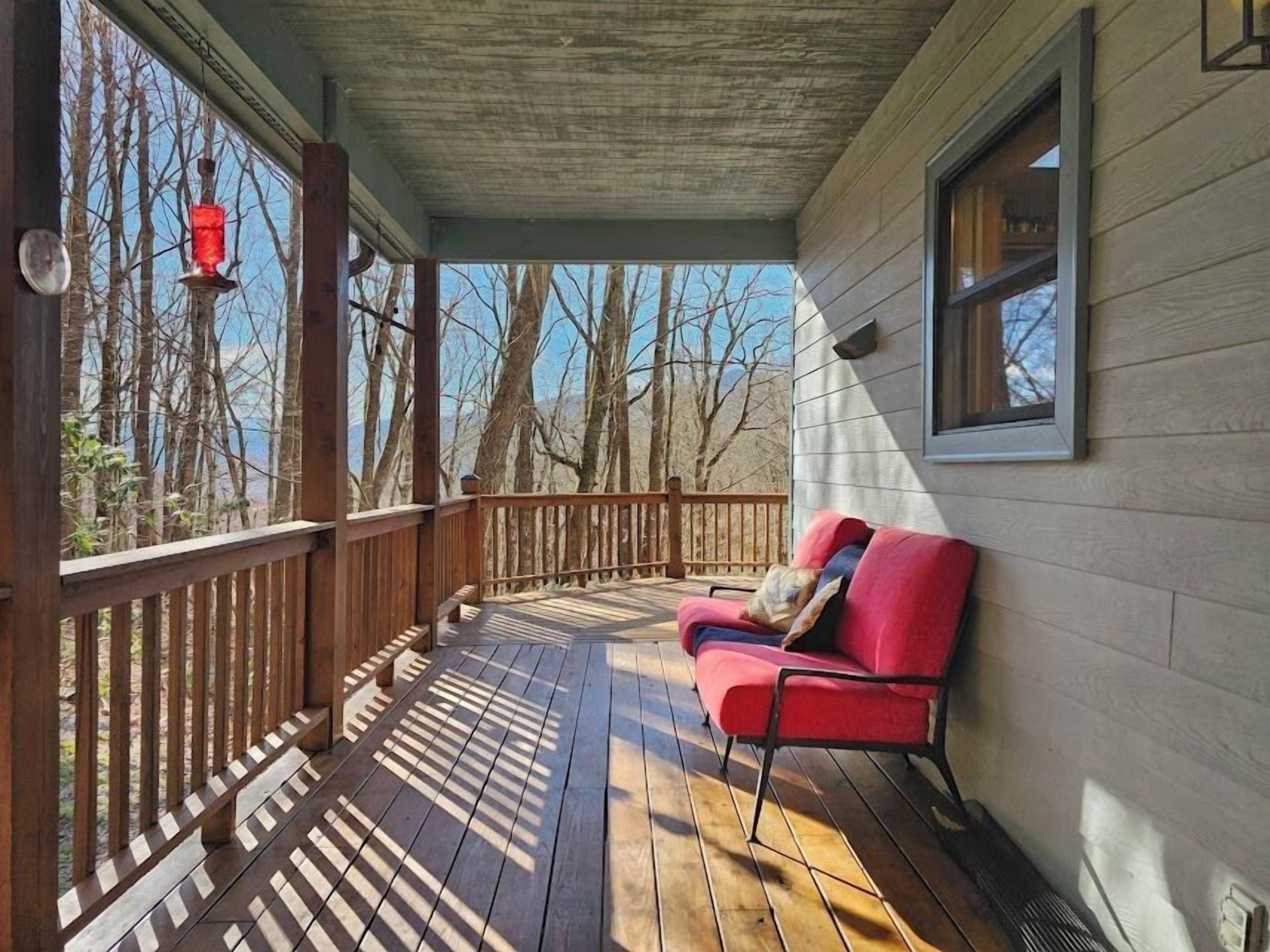 A wooden deck with a red bench, a hanging lantern, and a window overlooking a forested area.