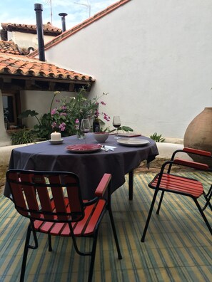 Une table à manger installée à l’extérieur, avec des chaises, une bougie, des verres à vin et un saladier.