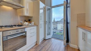 Une cuisine moderne équipée d’une cuisinière à gaz, d’un four et de meubles blancs. Une grande fenêtre offre une vue sur le paysage urbain.