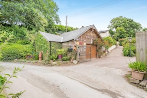 A wooden building with a sloped roof, a gated entrance, and a garden area with potted plants.