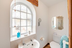 A bathroom with a large arched window, a sink, a toilet, and a mirror.